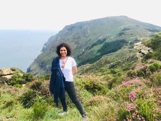 Dr. Karina Maldonado-Mariscal standing in a white T-Shirt at the edge of a cliff by the ocean on a sunny day