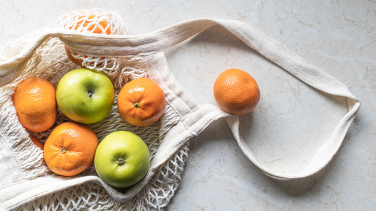 Einkaufsnetz, in und neben dem Orangen und Äpfel liegen