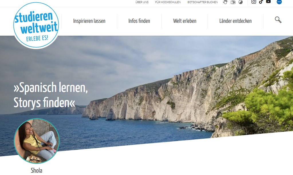im Hintergrund ist ein Bild von der spanischen Küste, mit einem blauen Meer und Felsen, die direkt am Wasser steil hochgehen. Ein kleines Foto von Shola steht im Verdergrund