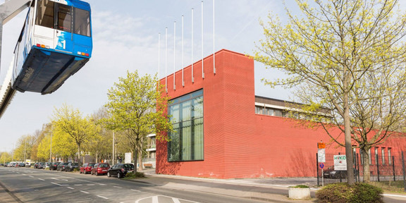 Das rot verklinkerte Internationale Begegnungszentrum auf dem Campus Nord. Im Vordergrund fährt die H-Bahn.