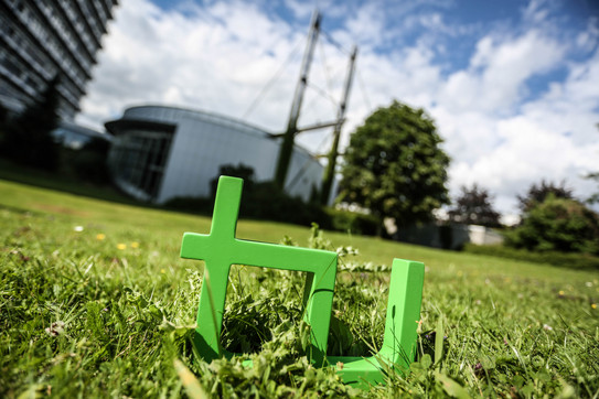 TU-Logo Im Vordergrund steht das TU-Logo im Gras, im Hintergrund das Audimax.