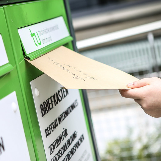 Eine Hand wirft einen Umschlag in den Fristenbriefkasten