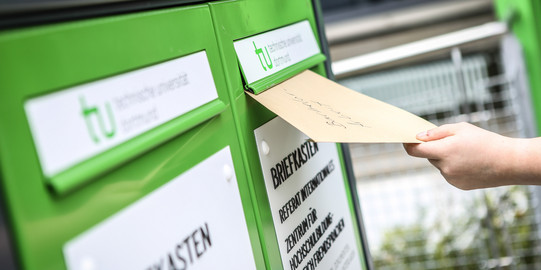 Eine Hand wirft einen Umschlag in den Fristenbriefkasten