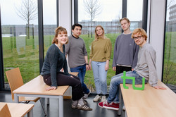 Five students sit on the table and stand together in a seminar room.