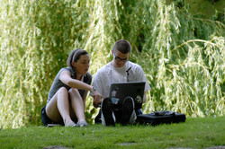 Two students are studying together with laptop on a meadow in summer
